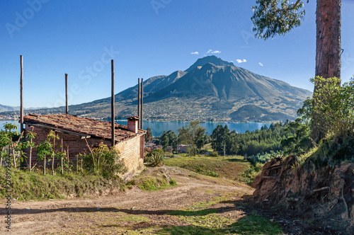 View of the Imbabura volcano, San Pablo lake, surrounding fields and a small cabin, on a clear morning. Ecuador