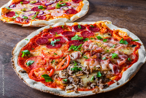 Pizza "Four Seasons" with Mozzarella cheese, ham, tomato sauce, salami, bacon, mushroom, pepper, Spices and Fresh basil. Italian pizza on wooden table background