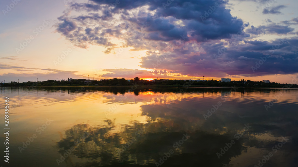 Wonderful sunset panorama over the city horizon with reflection on the calm lake water in a silent summer evening