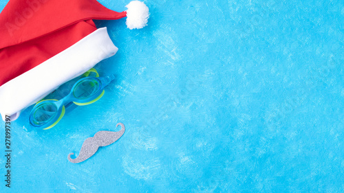 Banner. Hat of Santa Claus with goggles for swimming and a red lips. Christmas vacation, sandals and swimming glasses by water, slippers and pool goggles near swimming pool