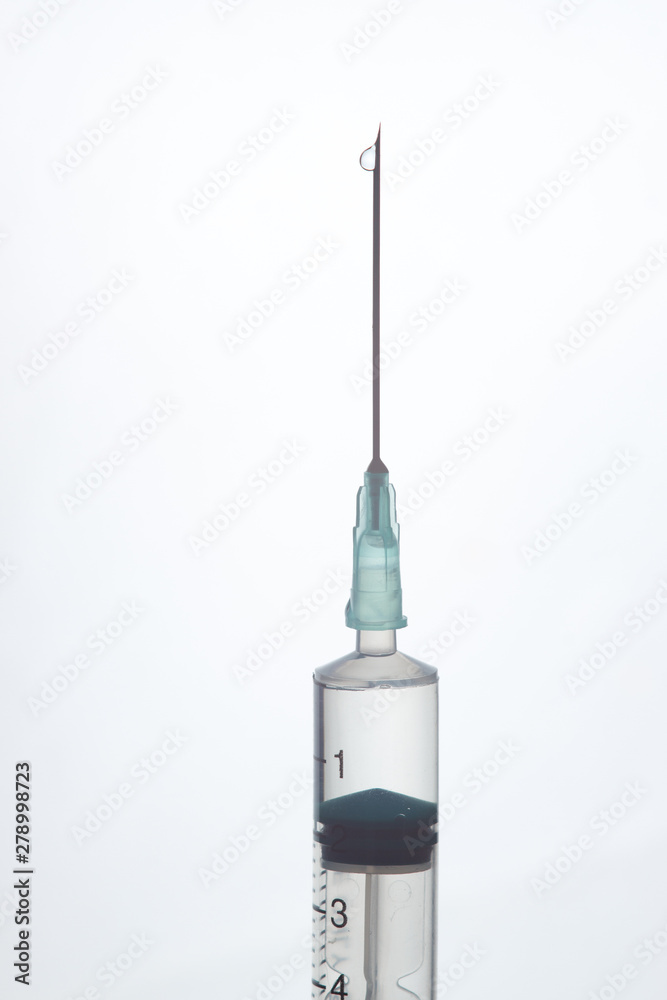 The end of the syringe with a needle filled with liquid on a light background. The end of the syringe with a needle filled with liquid on a light background.