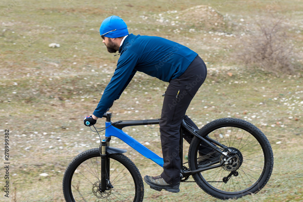 Obraz premium Cyclist in shorts and jersey on a modern carbon hardtail bike with an air suspension fork rides off-road on the orange-red hills at sunset evening in summer 