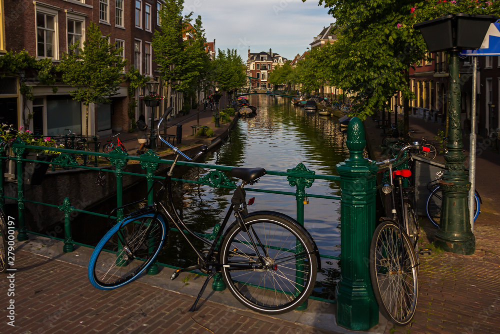Leiden, Holland, Netherlands, April 18, 2019, bicycles parked on a bridge and along a street, canal in Leiden old town. Flowers in a flowerbeds, boats on the water.