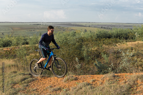 Cyclist in shorts and jersey on a modern carbon hardtail bike with an air suspension fork rides off-road on the orange-red hills at sunset evening in summer  © Mountains Hunter
