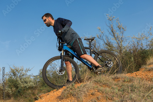 Cyclist in shorts and jersey on a modern carbon hardtail bike with an air suspension fork rides off-road on the orange-red hills at sunset evening in summer 