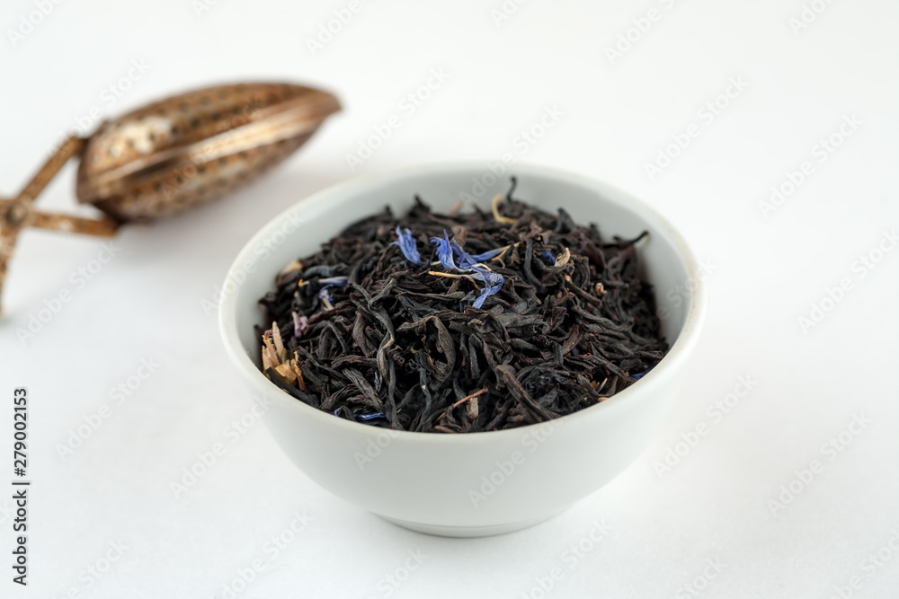 Fototapeta premium Dry black tea with blue flowers leaves in white bowl and metal tea spoon