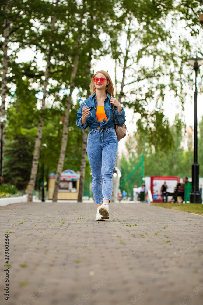Obraz premium Young Blonde woman in blue jeans walking in summer park