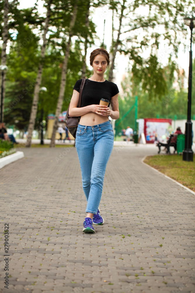 Young beautiful brunette girl in jeans and t-shirt walking in summer park