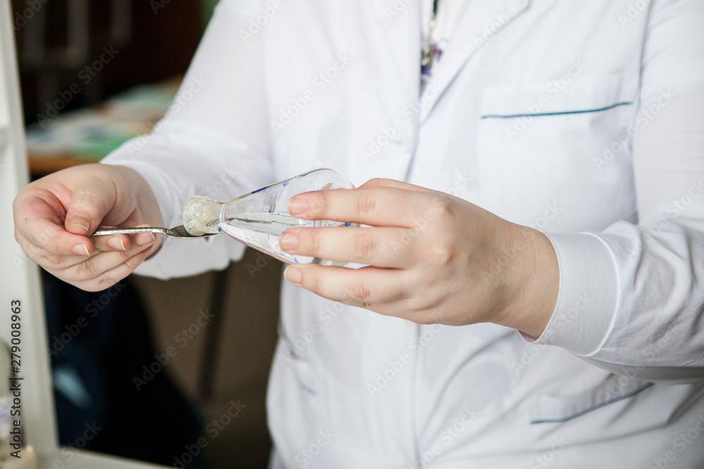 a female chemist in a lab pours a volatile liquid from a flask into a spoon a female chemist in a lab pours a volatile liquid from a flask into a spoon