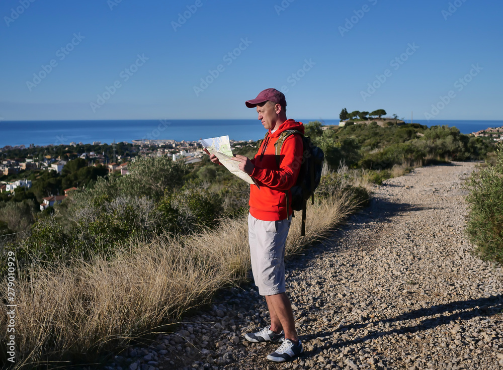 Tourist guy is standing on a hill path and holding a map