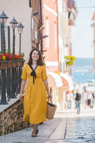 young pretty woman in yellow dress walking by small porec city streets sea on background