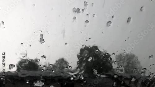 Hail and ice graupel falling on glass of rooftop window during hailstorm