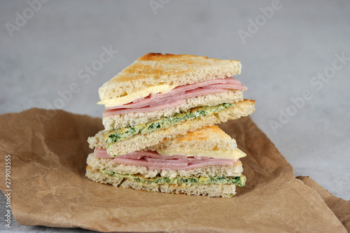 Sandwiches of white bread on Kraft paper. Sandwich stuffing consists of ham, cheese and scrambled eggs with spinach. Close-up.