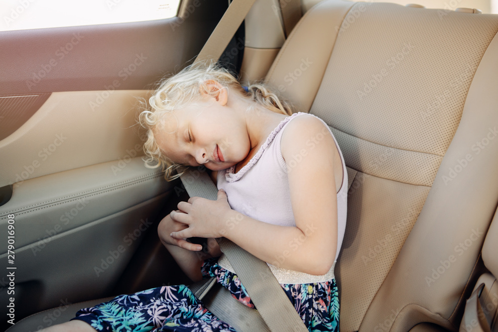 Portrait of adorable cute white Caucasian preschool girl child sitting in car seat . Sleeping kid in automobile vehicle fastened with seat belt. Care and protection of children on roads.