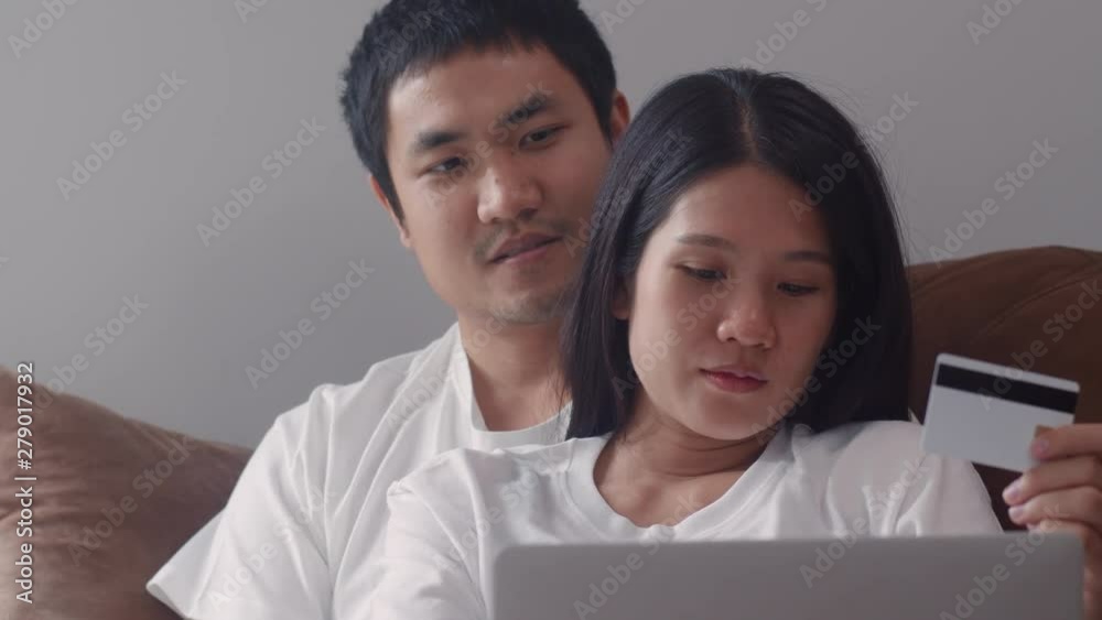 Young Asian Pregnant couple online shopping at home. Mom and Dad feeling happy using laptop technology and credit card buying baby product while lying on sofa in living room at home concept. Young Asian Pregnant couple online shopping at home. Mom and Dad feeling happy using laptop technology and credit card buying baby product while lying on sofa in living room at home concept.
