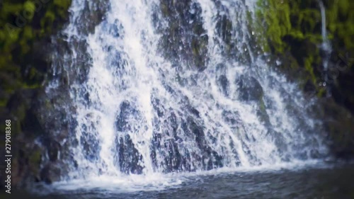 Close up shot in slow-motion of a waterfall. Clear blue and white water and green moss around it. photo