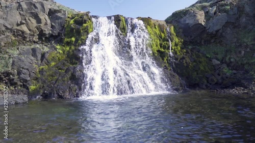 Slow-motion capture of a waterfall in green moss and stone cliff. Sunny day in rural Iceland. photo