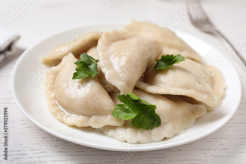 Plate of tasty cooked dumplings served on white wooden table, closeup