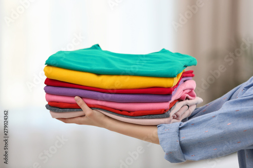 Woman holding folded clean clothes indoors, closeup. Laundry day