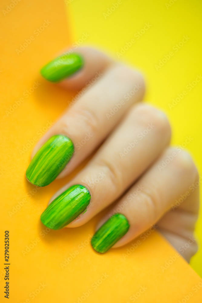 Young woman's hand with beautiful manicure on yellow background holding orange color paper close up Young woman's hand with beautiful manicure on yellow background holding orange color paper close up