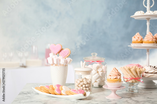 Candy bar with different sweets on white marble table against color background