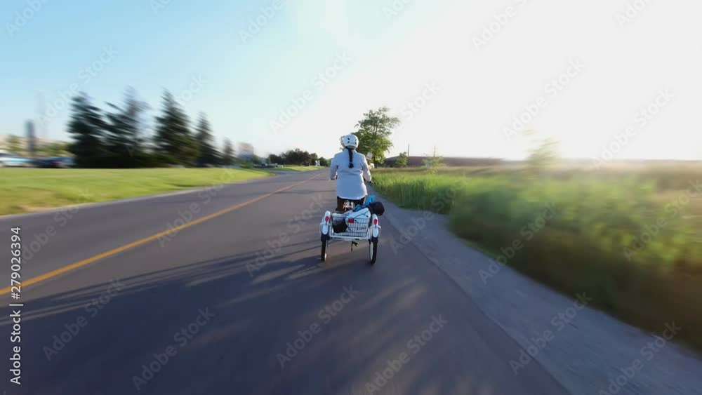 Woman ridding bicycle with three wheels view from behind. Cyclist riding at city road in the evening. Commuter bike activity in the sun set. 4k. Woman ridding bicycle with three wheels view from behind. Cyclist riding at city road in the evening. Commuter bike activity in the sun set. 4k.