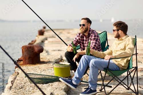leisure and people concept - happy friends fishing and drinking beer on pier