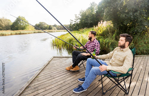 leisure and people concept - male friends fishing and drinking beer on lake