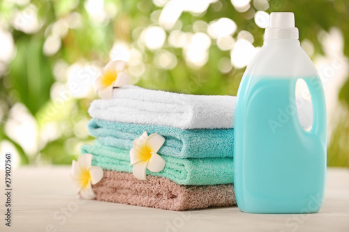 Pile of fresh towels, flowers and detergent on table against blurred background photo