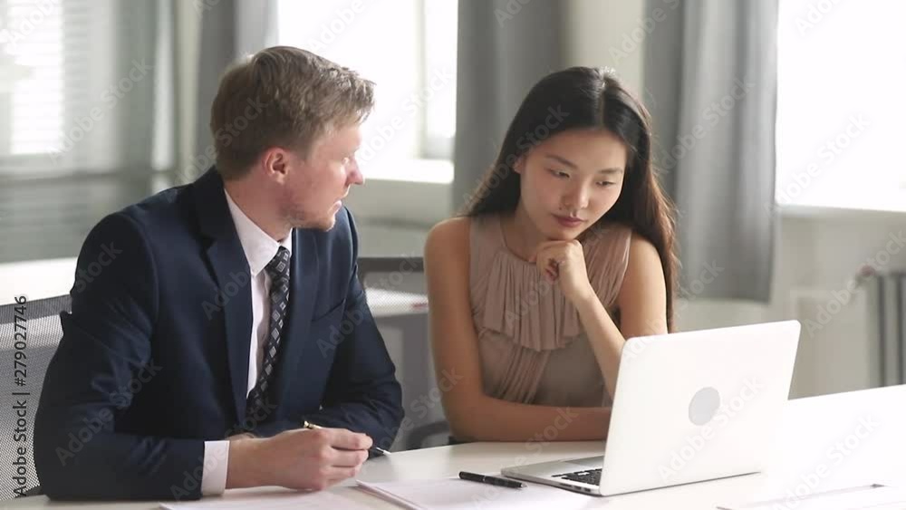 Helpful caucasian boss pointing at laptop teaching female asian intern Helpful caucasian boss pointing at laptop teaching female asian intern