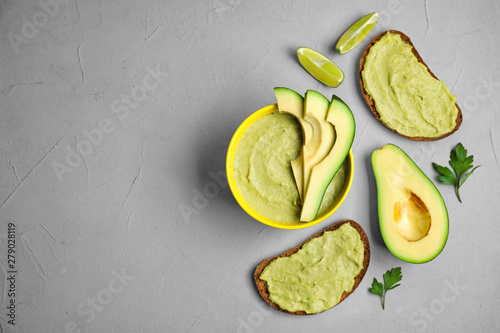 Flat lay composition with bowl of guacamole made of ripe avocados on grey table. Space for text