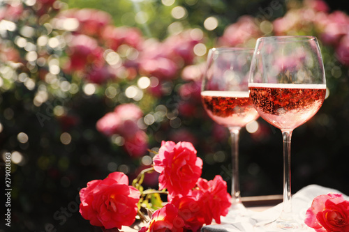 Fototapeta Naklejka Na Ścianę i Meble -  Glasses of rose wine on table in blooming garden, space for text