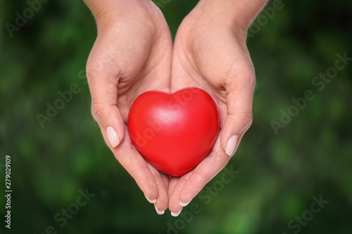 Young woman holding red heart on blurred green background  closeup. Donation concept