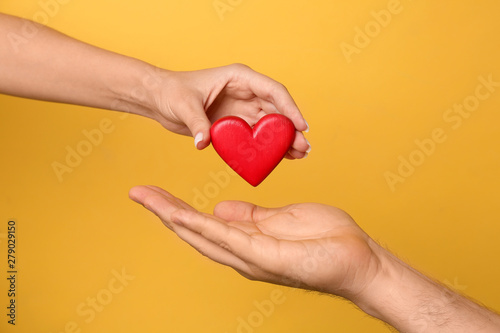 Woman giving red heart to man on yellow background, closeup. Donation concept photo
