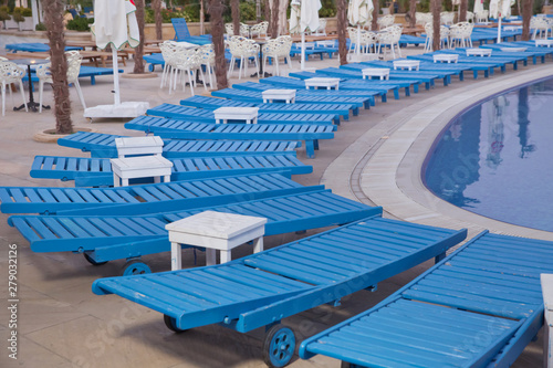 Lounge sunbeds near swimming pool .Sun loungers by the pool  blue  comfortable atmosphere .Swimming pool beds in nature. Empty sunbeds by the beautiful resort pool .