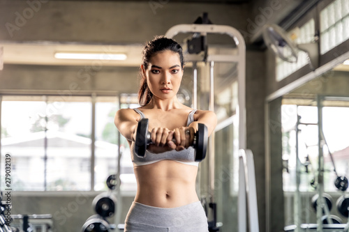 Asian beautiful woman is lifting double in the gym, She smile happily in exercise because it makes her shapely, the concept of exercise, lose weight, strengthen muscles.