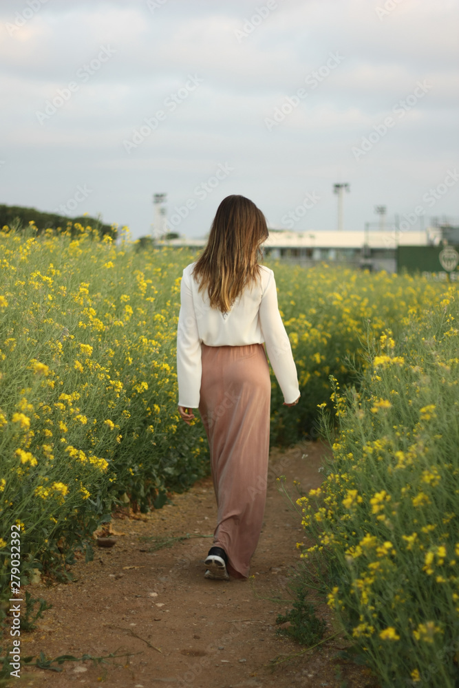 Fototapeta premium Beautiful woman on yellow flowers field with dark cloudy sky