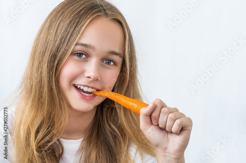 Beautiful smiling girl with long hair in a white shirt bites carrots isolated on white background