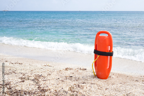 Orange buoy standing on the sand in front of the sea, safety concept