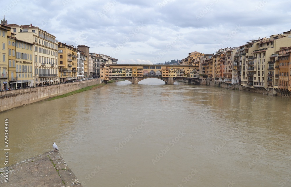 View of the Ponte Vecco bridge, ancient buildings and the Arno River in Florence on an overcast day.