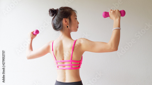 Bodybuilding. Strong fit woman exercising with dumbbells. Muscular Asian girl in pink sexy sportswear lifting weights and doing exercise for arms, back view studio shot on white background.