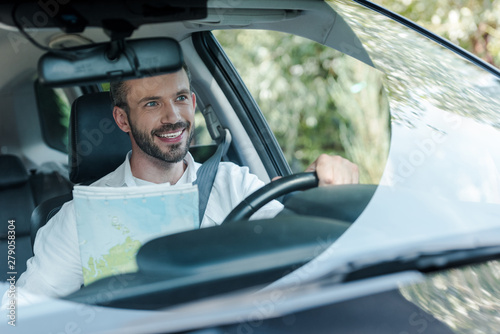 selective focus of bearded and happy man driving car and looking at map