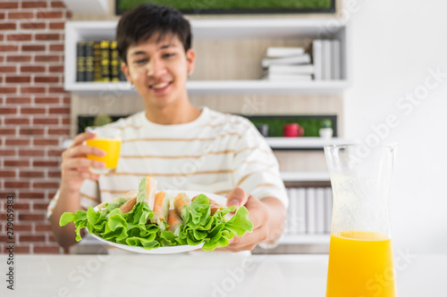 A young Asian man holding a plate of vegetable snack roll and a glass of orange juice.