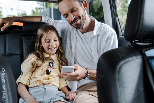 selective focus of happy man using smartphone near daughter in car