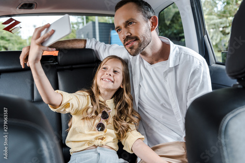 selective focus of happy kid talking selfie with father in car