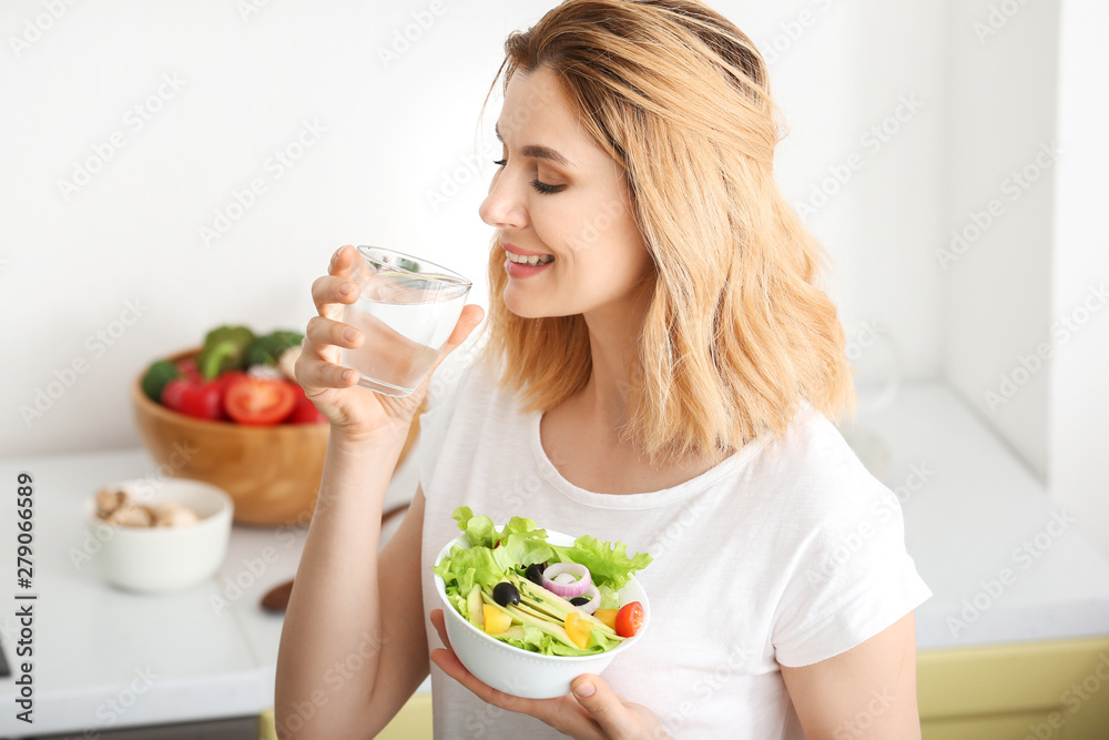 Woman with healthy vegetable salad and glass of water in kitchen Woman with healthy vegetable salad and glass of water in kitchen