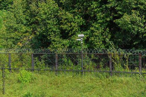 Surveillance camera on a metal fence with barbed wire.