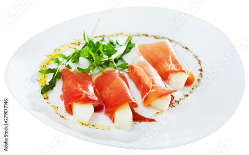 Tasty dish rolls of prosciutto di parma with melon served with arugula at plate