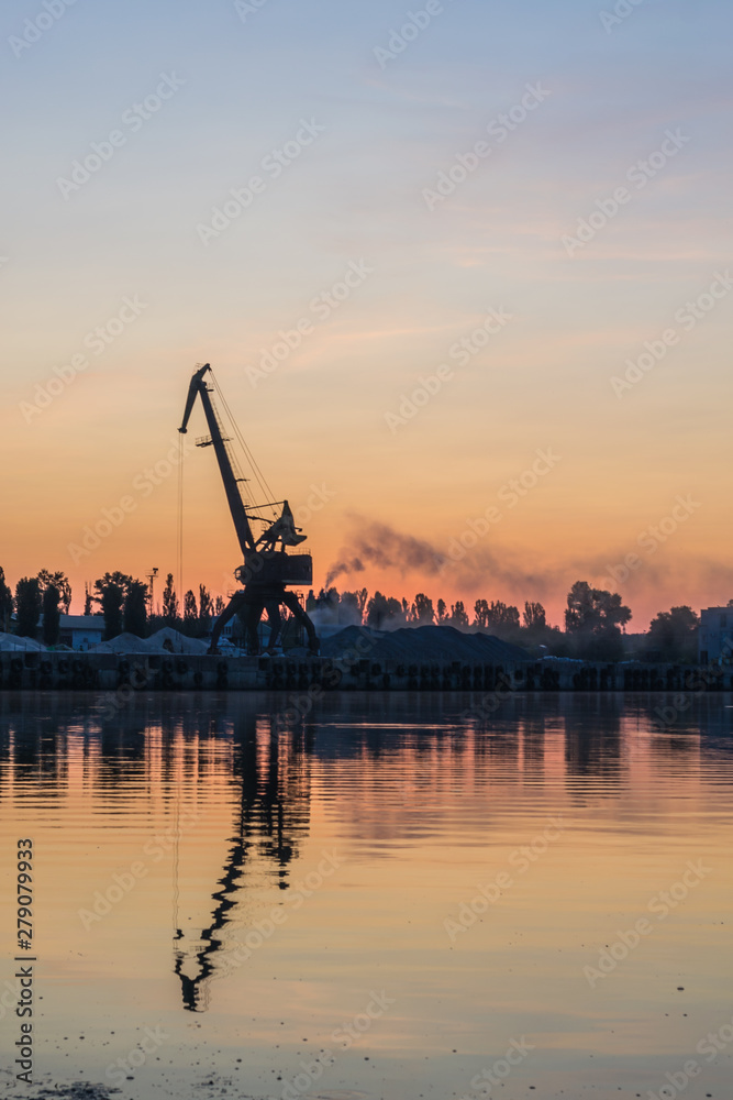 Sunrise over the port. Dawn over the river. The cranes in the industrial part of the city on the shore.