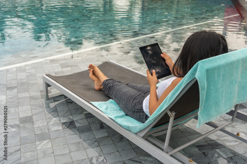 Woman using tablet and relaxing at swimming pool in summer